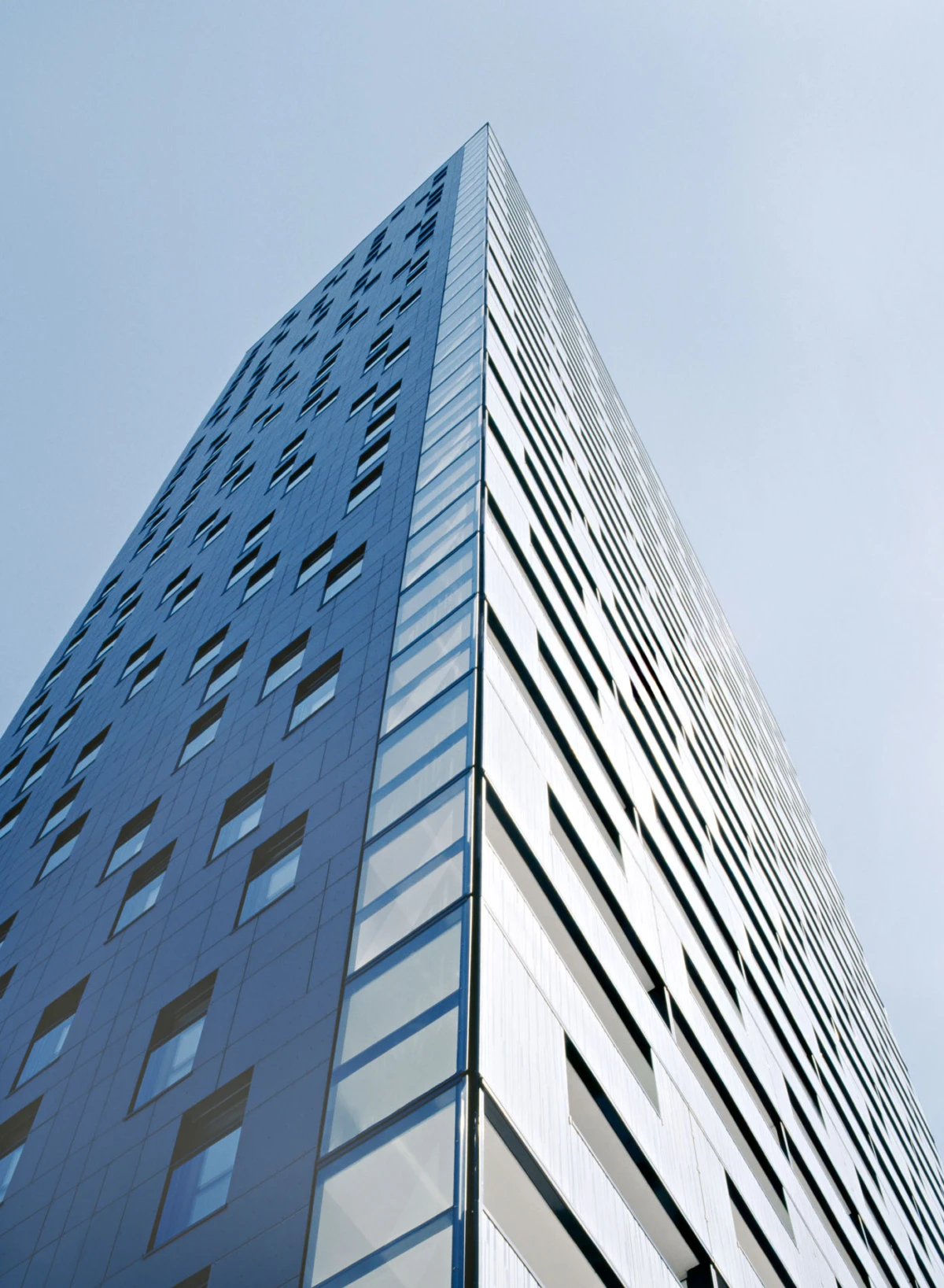 Tall glass skyscraper viewed from ground level, ascending toward a clear blue sky.