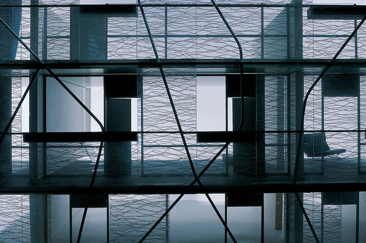 Interior of a modern building with crisscrossing metal framework and glass walls; a lonely chair visible in the background.