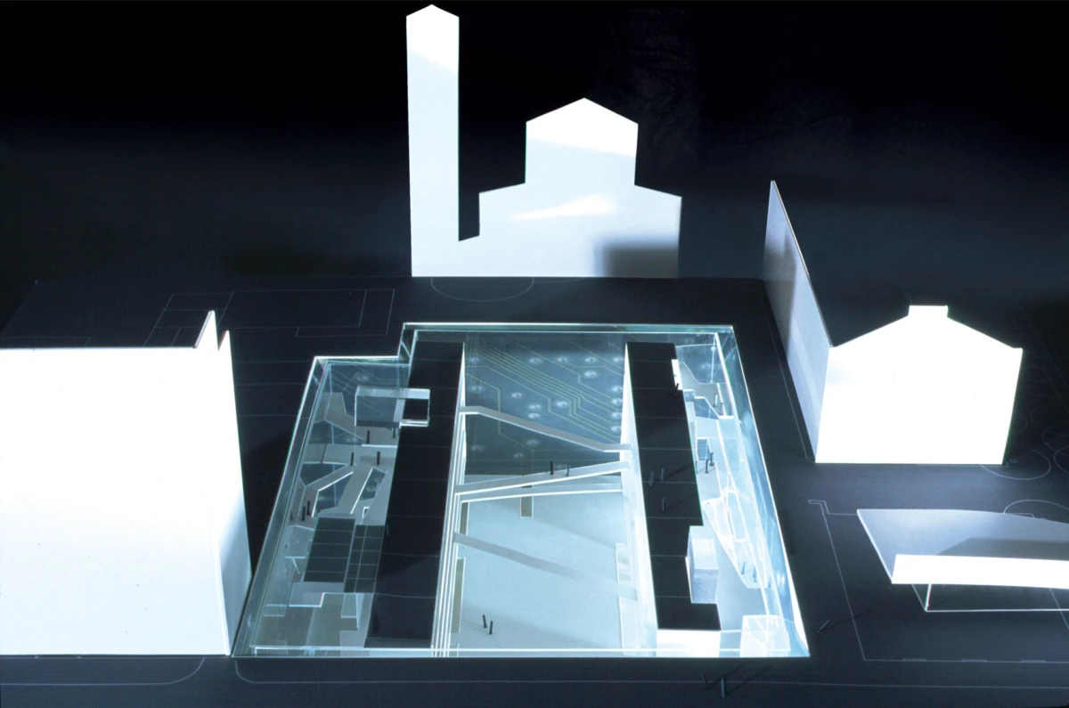 Architectural scale model of a modern complex with a central glass atrium, visible staircases, and surrounding white block buildings.