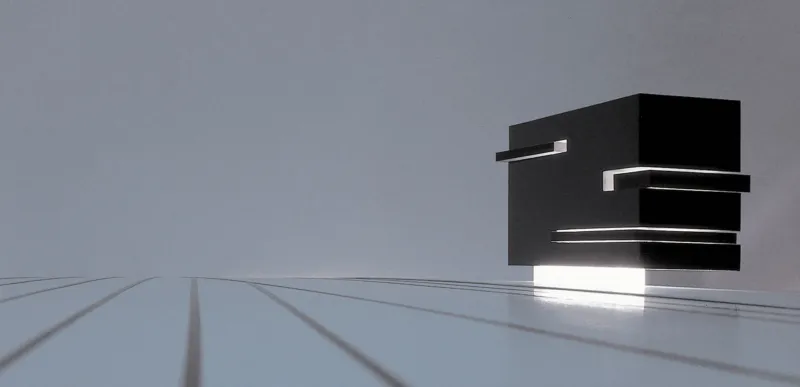 Abstract sculpture of stacked black rectangular blocks on a reflective glass surface against a gray sky.
