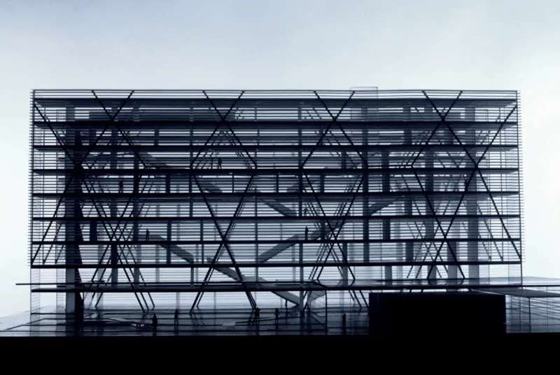 Modern glass-fronted building with crisscross steel framework; interior stairs visible and silhouettes of people on multiple floors.