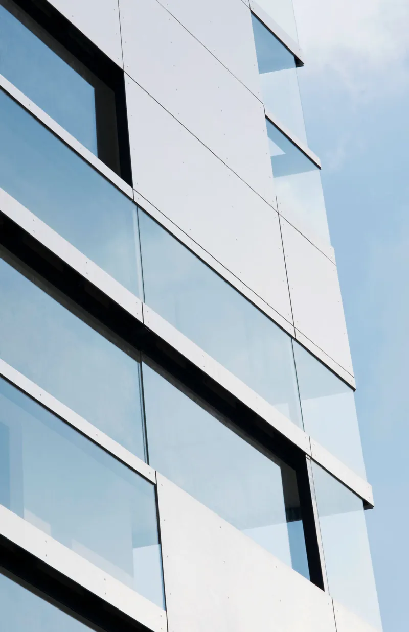 Exterior view of a modern glass-clad office building with white panels, angled windows from a low vantage.