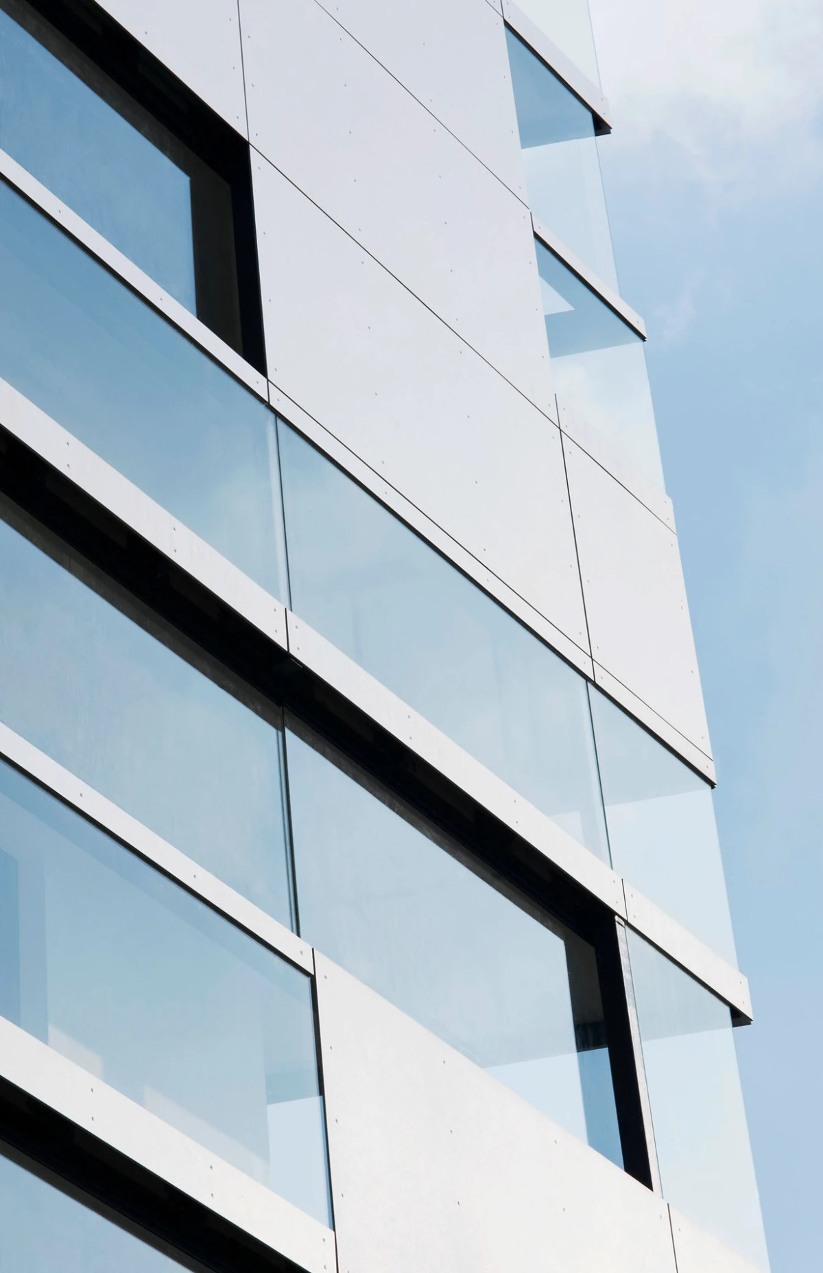 Exterior view of a modern glass-clad office building with white panels, angled windows from a low vantage.