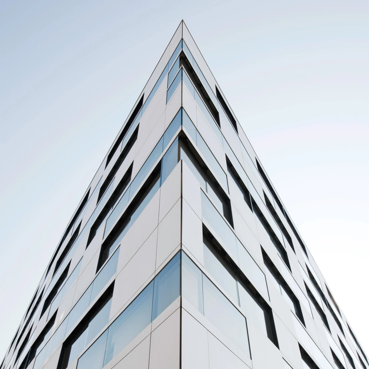 Corner view of a modern glass-clad office building, photographed from the ground up, highlighting its angular façade and large windows.