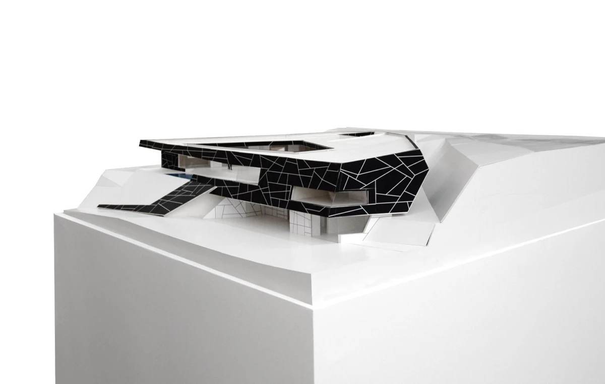 Scale architectural model of a black, mosaic-faceted building atop a white pedestal against a white background.