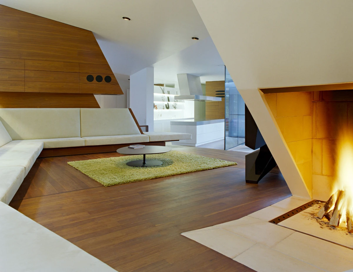 Modern living room featuring a white sectional sofa, round coffee table on a green rug, wooden floors, and a lit fireplace.