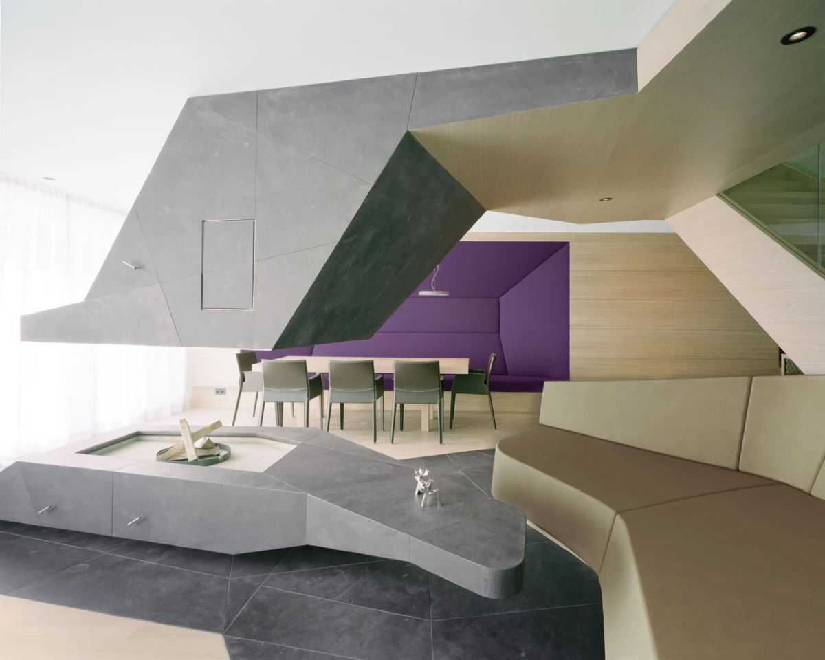 Contemporary living room with a large angular concrete sculpture, purple alcove seating, wooden dining table with gray chairs, and beige curved sofa.