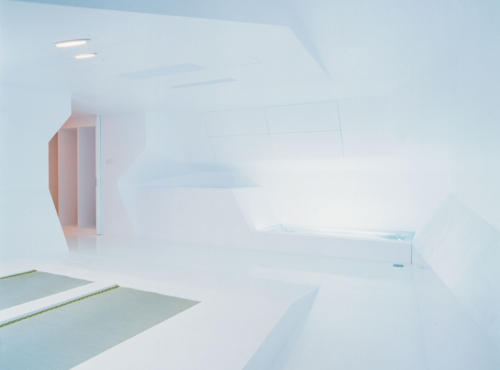 Minimalist white spa room with angular walls and a rectangular built-in tub along the right wall.