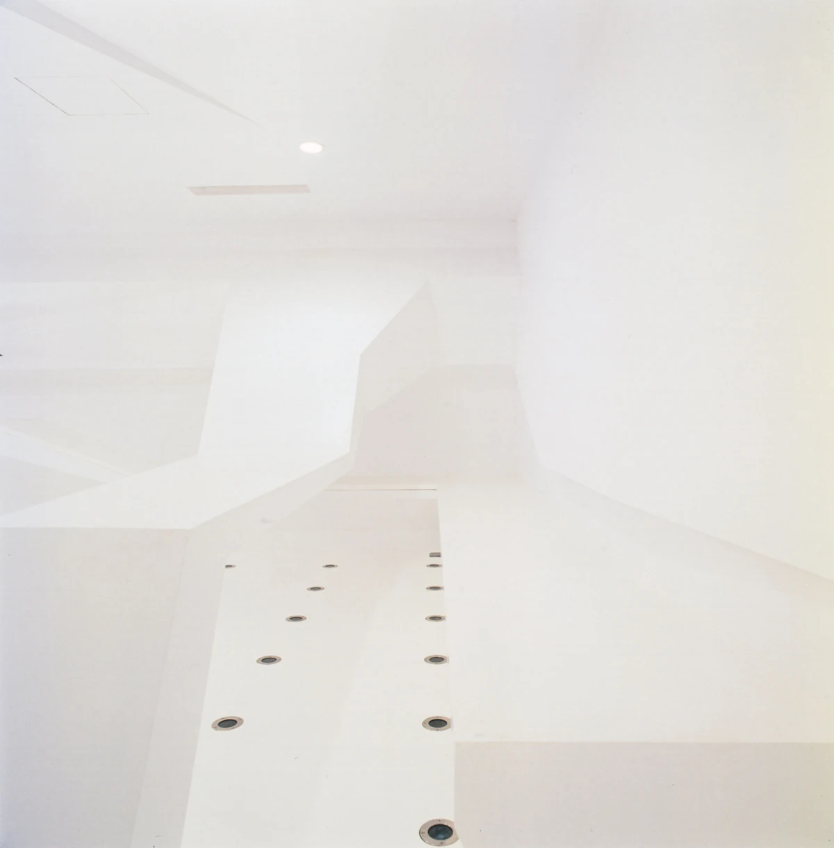 White minimalist interior with angular walls; a long elevated ledge dotted with circular recessed holes.