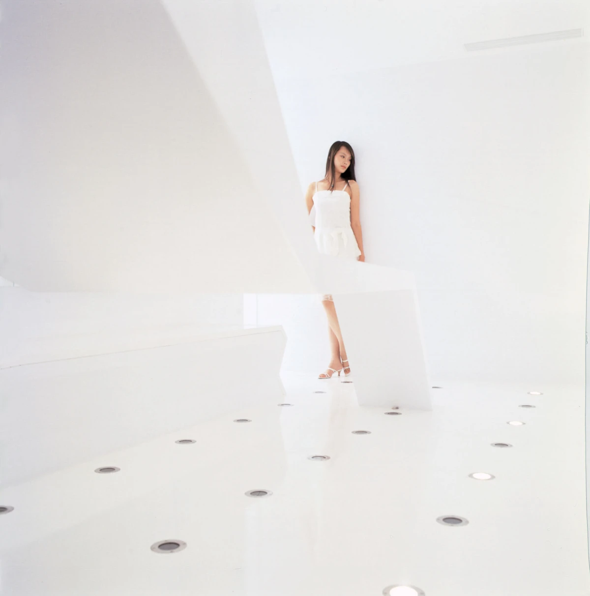 Person in a white dress and heels stands in a stark white, curved architectural space.