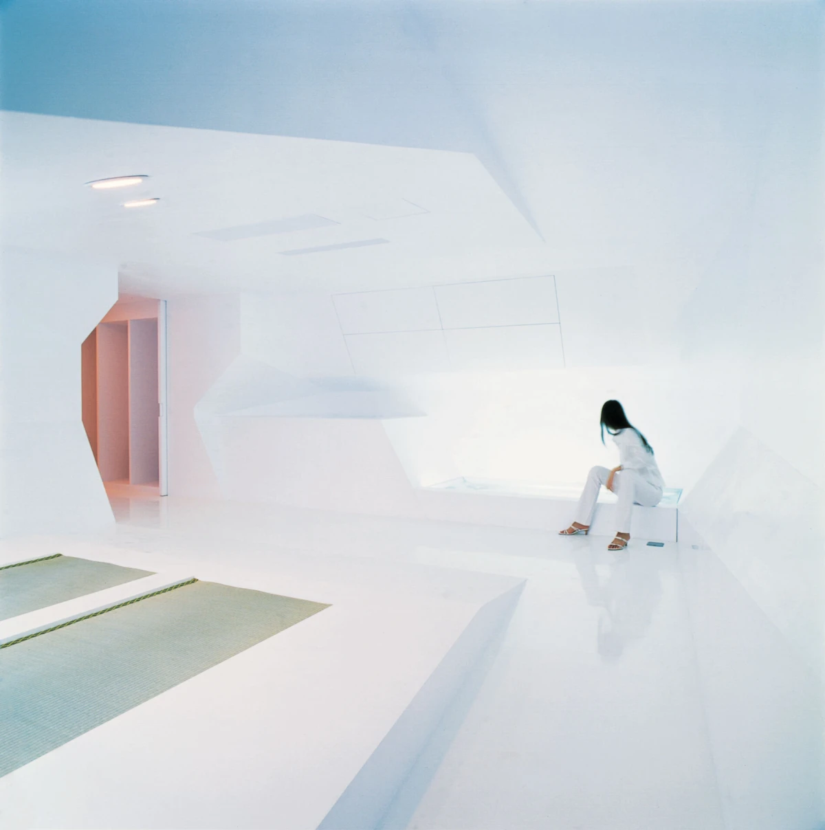 Person in white sits on a white bench inside a minimalist, futuristic white room.