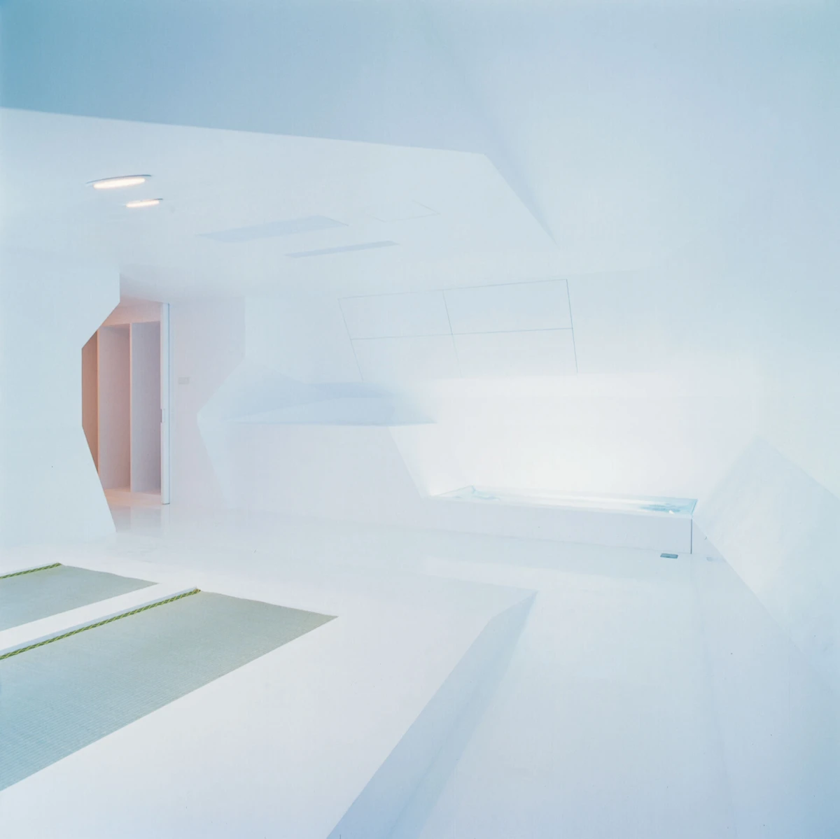 Minimalist white spa room with angular walls and a rectangular built-in tub along the right wall.