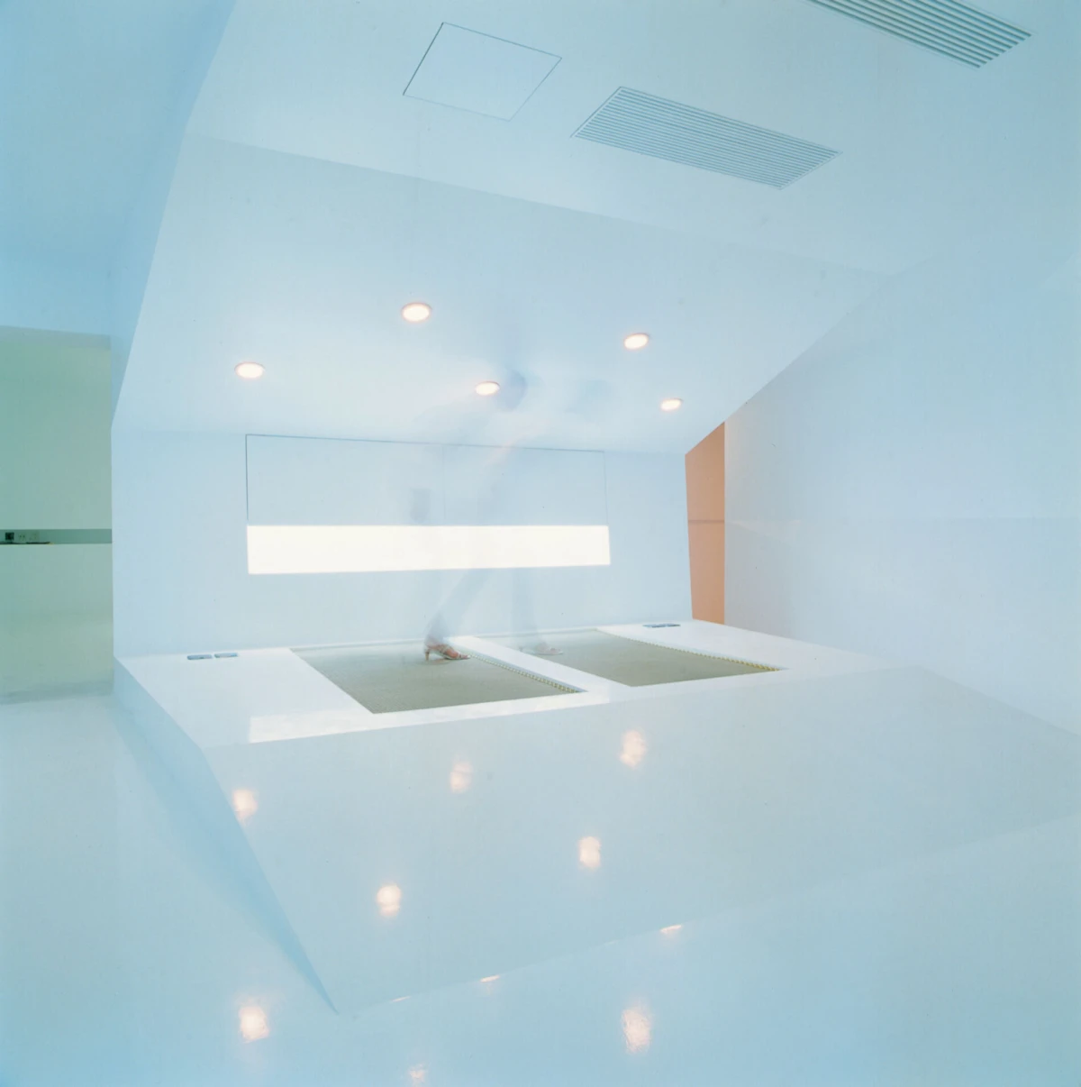 A person bending over two sunken rectangular basins in a bright white sterile room.