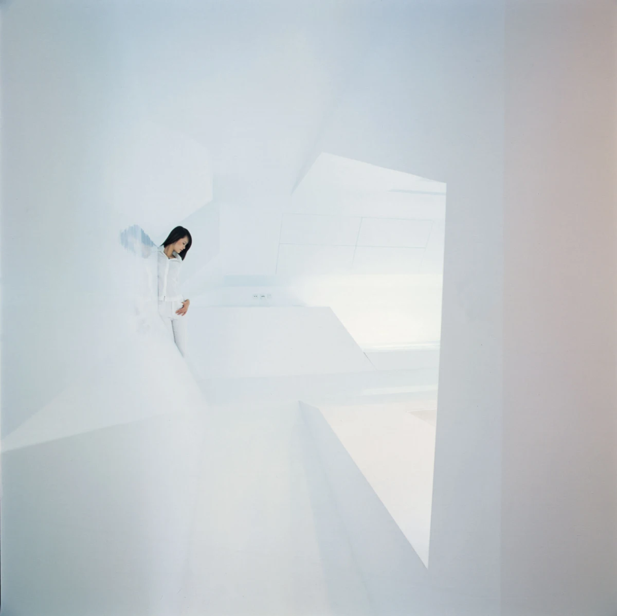 Person in white attire leaning against a white angular wall in a bright minimalist interior.