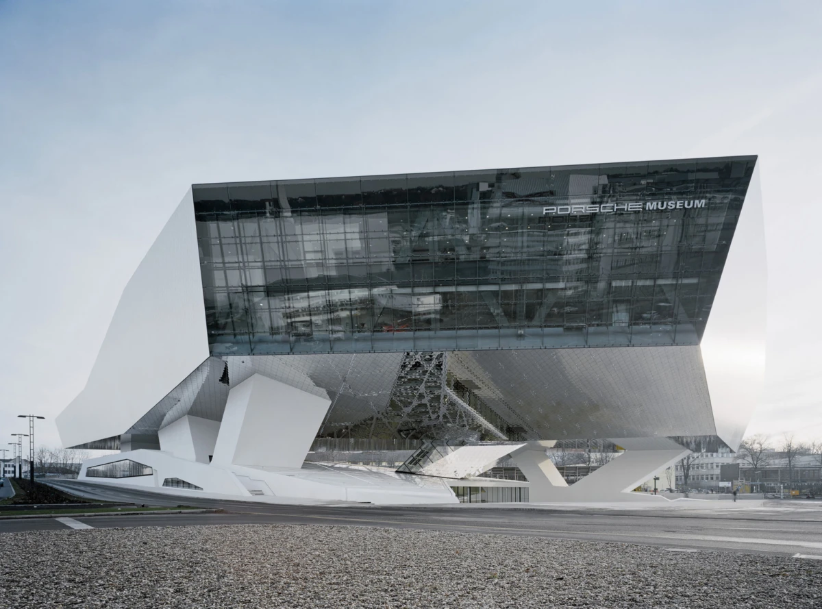 Exterior view of a modern white Porsche Museum building with angular supports and glass facade.
