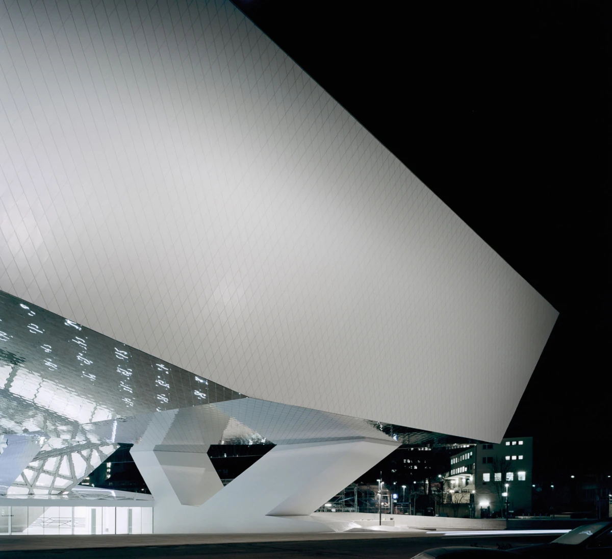 Night view of a white angular building with intersecting planes, towering over a reflective pool.