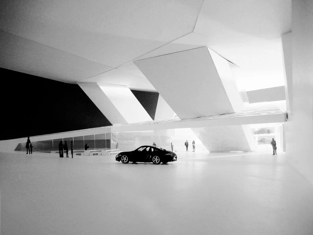 Black sports car parked in a minimalist, angular exhibition hall with large geometric structures and several visitors.
