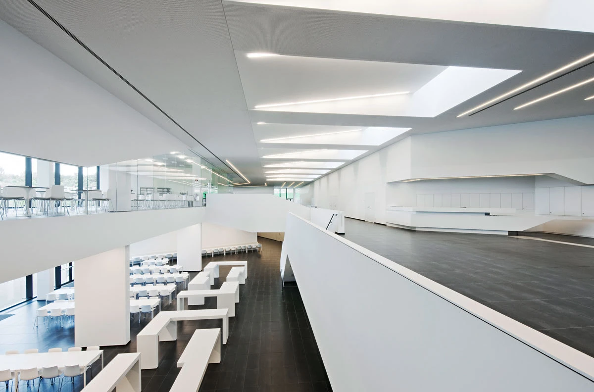 Interior of a spacious, empty modernist atrium with white walls, black flooring, glass balustrade, and minimalist seating.