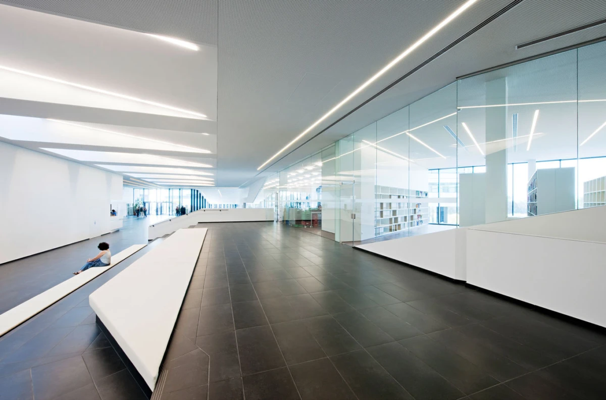 Person sitting on a long white bench in a bright, modern library atrium with glass walls.