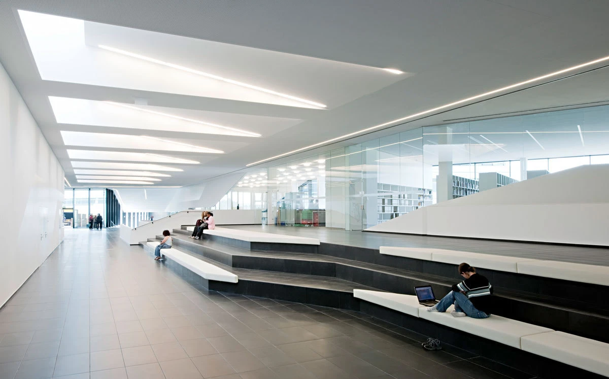 Person sitting on white tiered benches in a bright, modern atrium, using a laptop.
