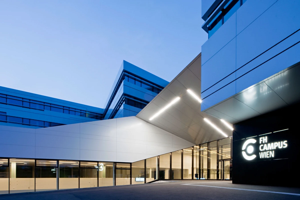 Modern campus building exterior at dusk with illuminated entrance and FH Campus Wien signage.