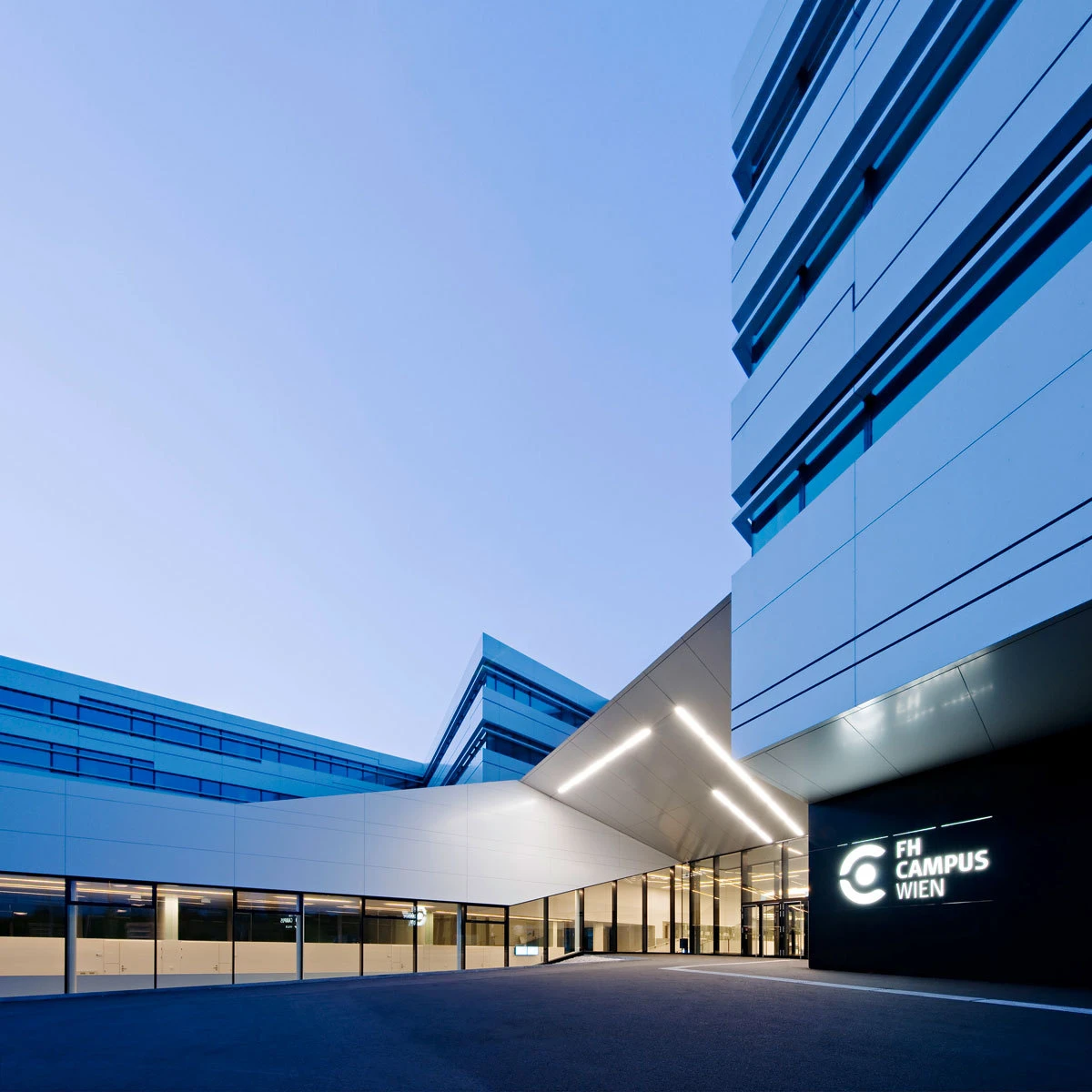 Modern campus building exterior with glass entrance and illuminated canopy; FH Campus Wien sign.