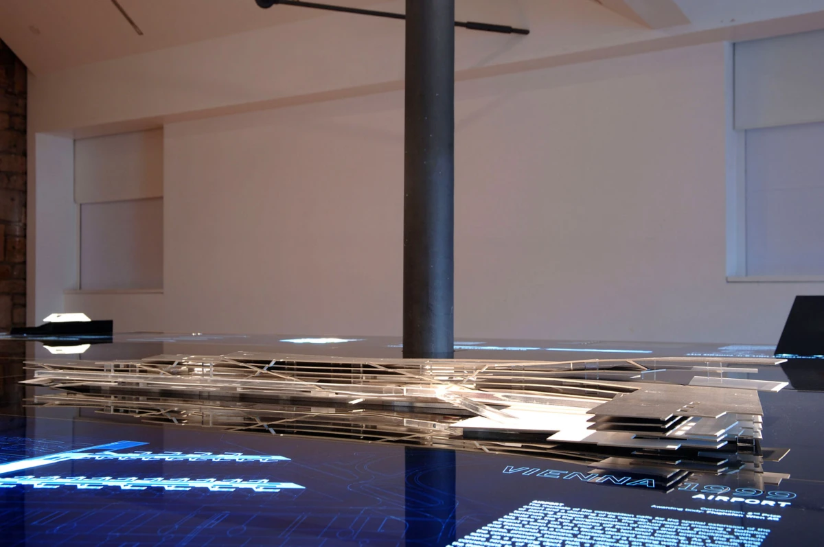 Layered thin metal sheets arranged around a central dark column in an indoor gallery.