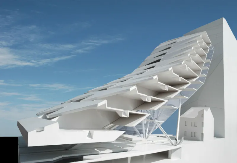 White futuristic building with stepped cantilevered balconies along a curved diagonal facade against a blue sky.