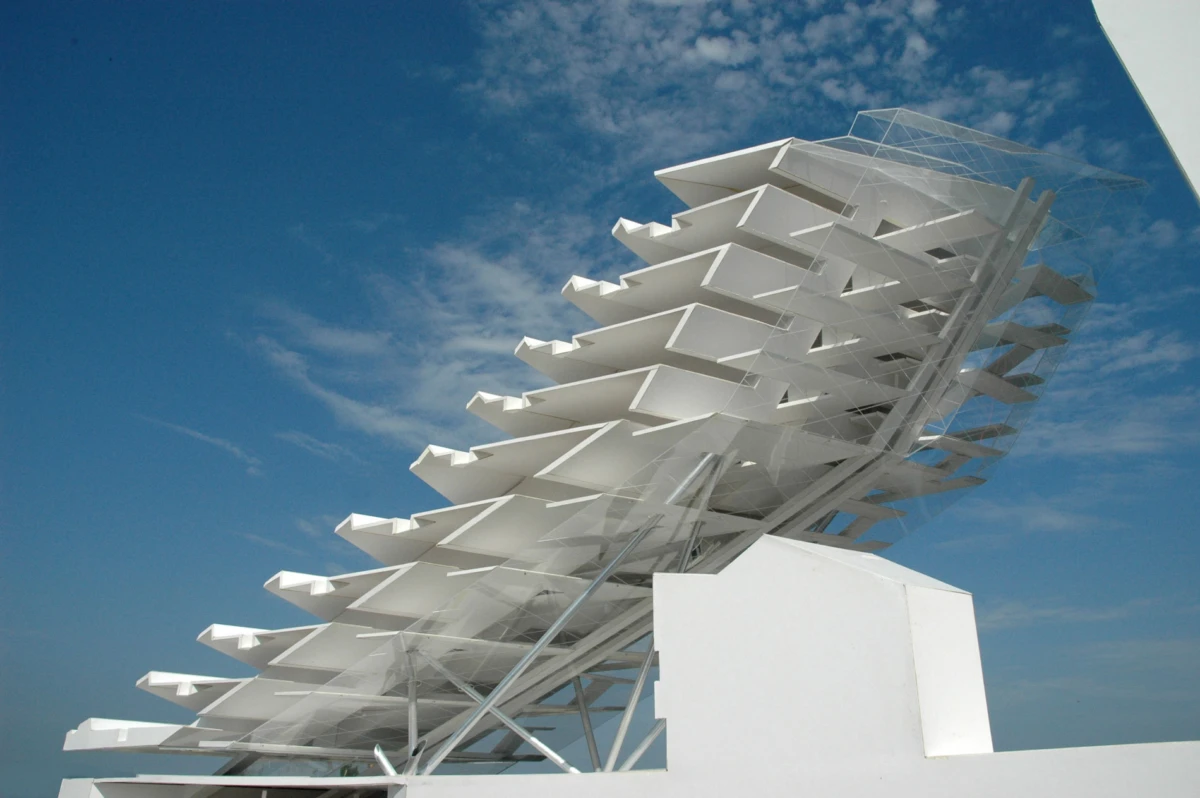 White architectural sculpture of diagonal stacked louvers on a metal frame under a blue sky.