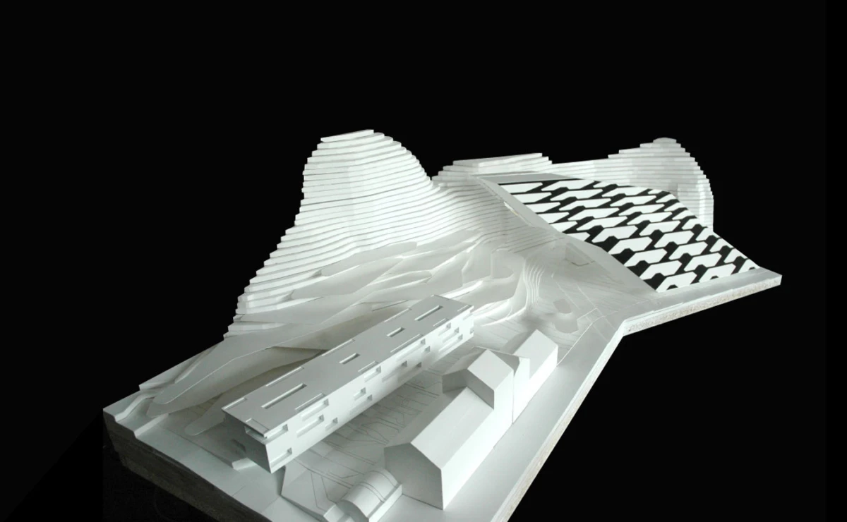 White architectural model of a landscape with stepped hills, a long rectangular building, and a checkered terrace.