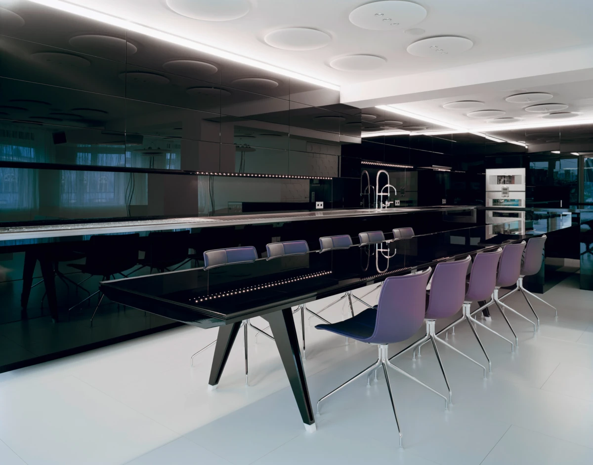 Modern kitchen bar area with a glossy black counter, purple chairs, and chrome faucets along a long island.