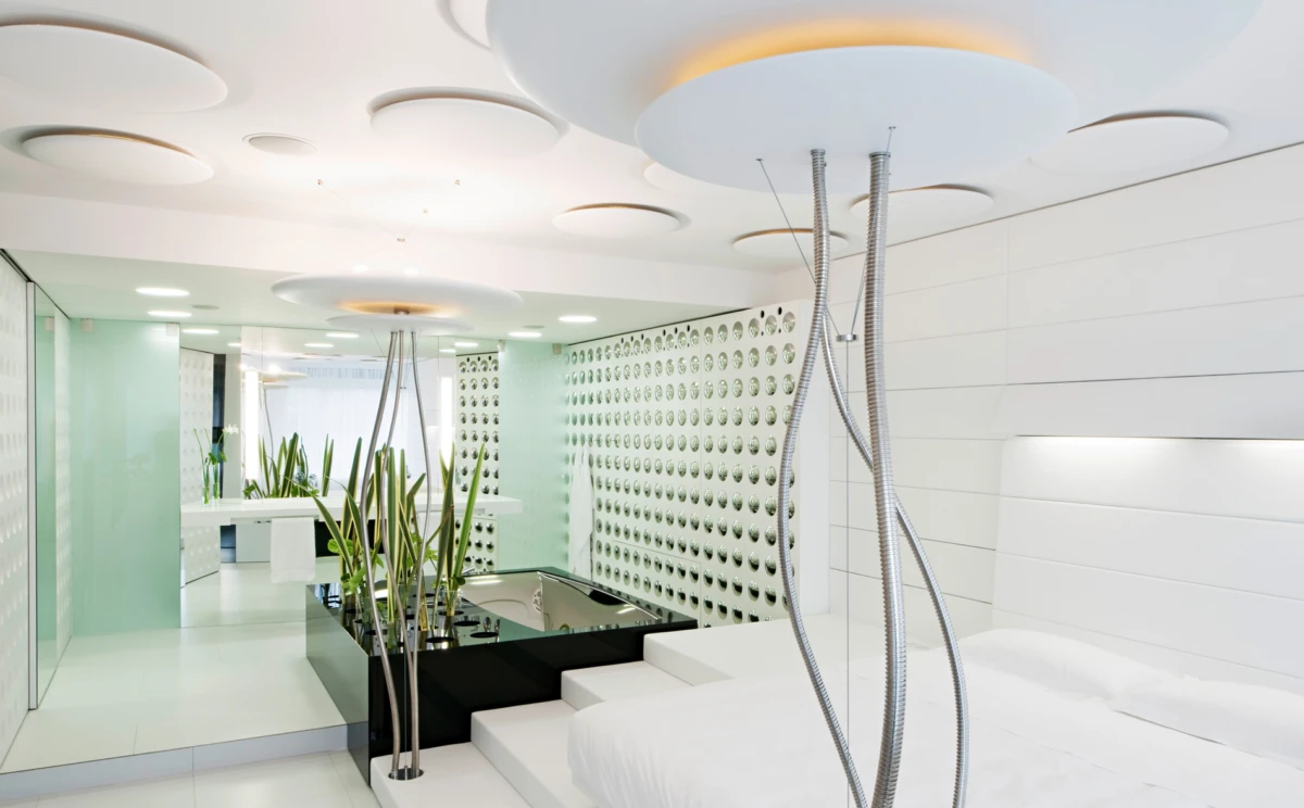 Contemporary spa-bedroom with white bed, sunken black pool, metal shower hoses, and tall planters.