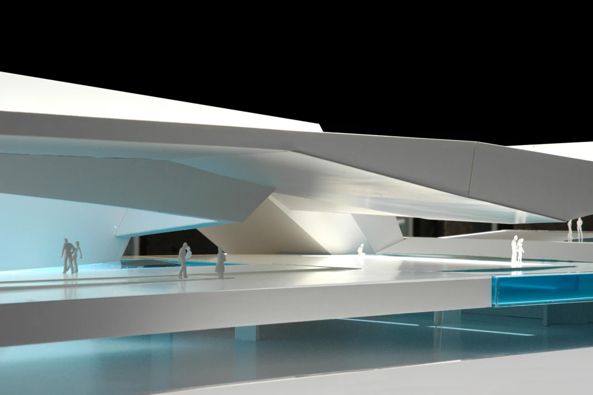 Scale model of a futuristic white architectural structure with tiny human figures on elevated walkways beside blue water features.