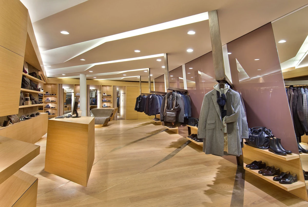 Gray wool overcoat on mannequin in a modern wooden clothing store; coats displayed on racks and leather shoes on shelves.