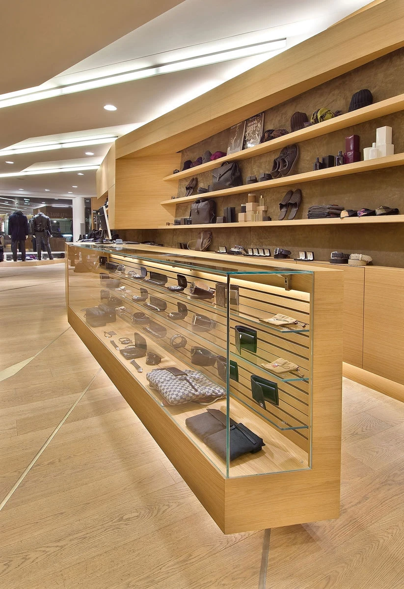 Wooden glass-front display counter in a boutique fashion store, showcasing wallets, bags, and shoes.
