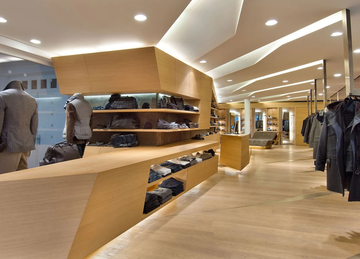 Interior of a modern clothing boutique with wooden shelves and counters, mannequins displaying jackets, and coats on racks.
