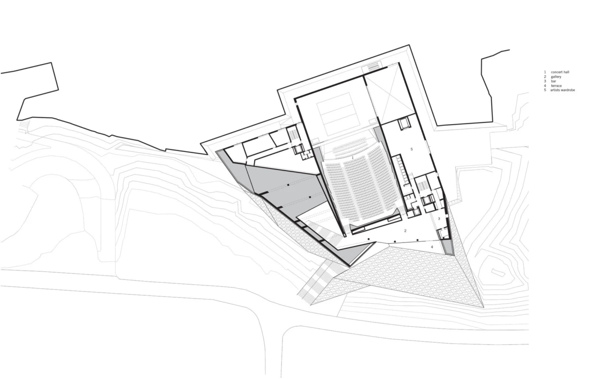 Plan view of a triangular building with an auditorium and seating, on a sloped site with contour lines and access paths.