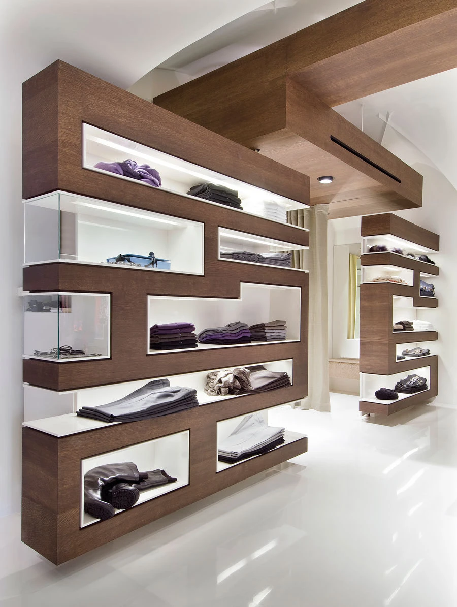 Modern clothing store interior with brown wood display units and white backlit shelves displaying folded garments.
