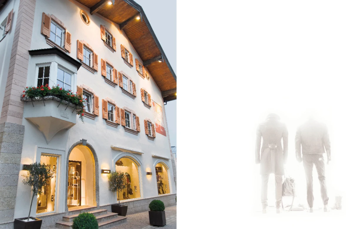 European-style hotel facade with arched entrances and flower boxes; on the right, faded silhouettes of two travelers standing with luggage.