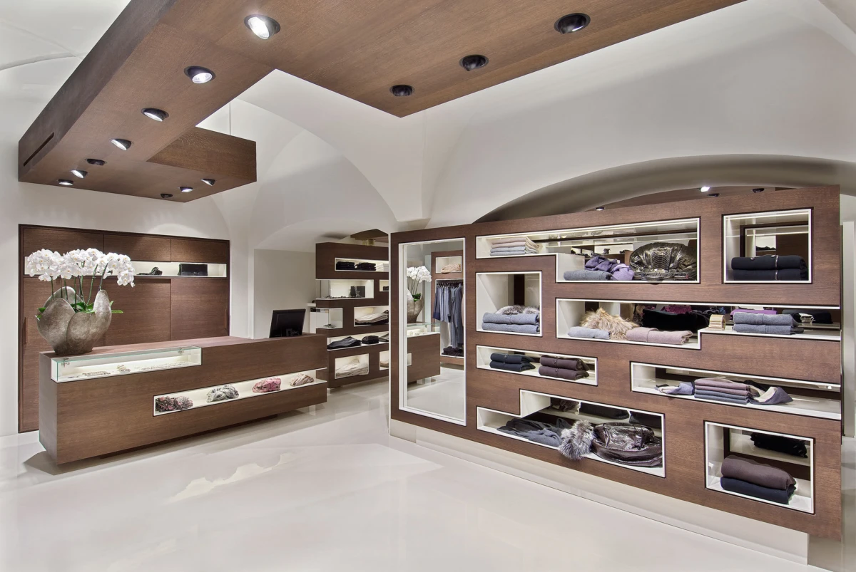 Modern clothing boutique with brown wood display walls showcasing folded fabrics and accessories; central counter and white floor.