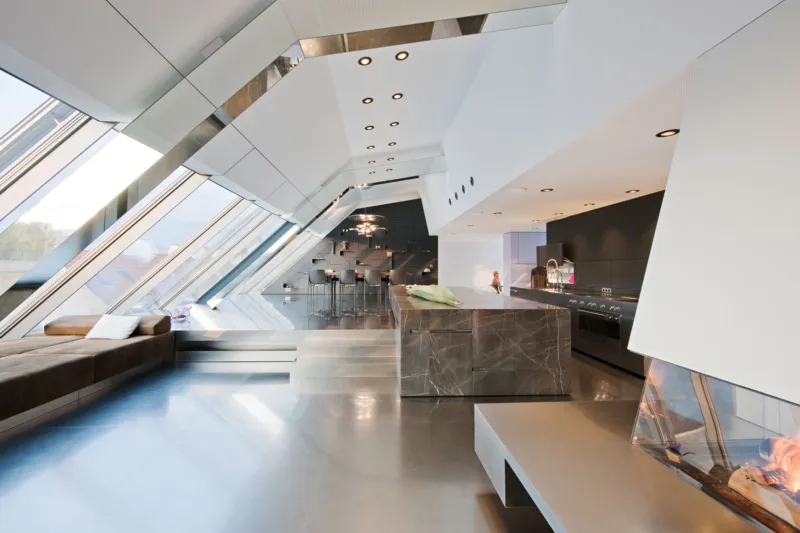 Empty futuristic open-plan living space with angular white walls, slanted glass windows, marble kitchen island, and fireplace.