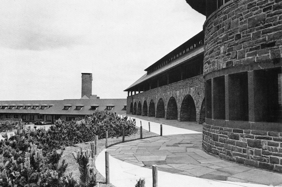 Stone fortress with arched arcade along a curved walkway; circular tower on the right, shrubs in the foreground.