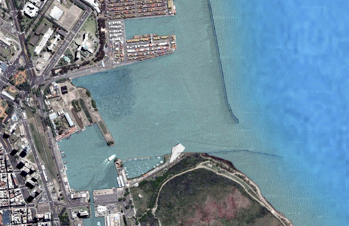 Aerial view of a harbor with docks, container ships, and a curved breakwater beside a green peninsula.