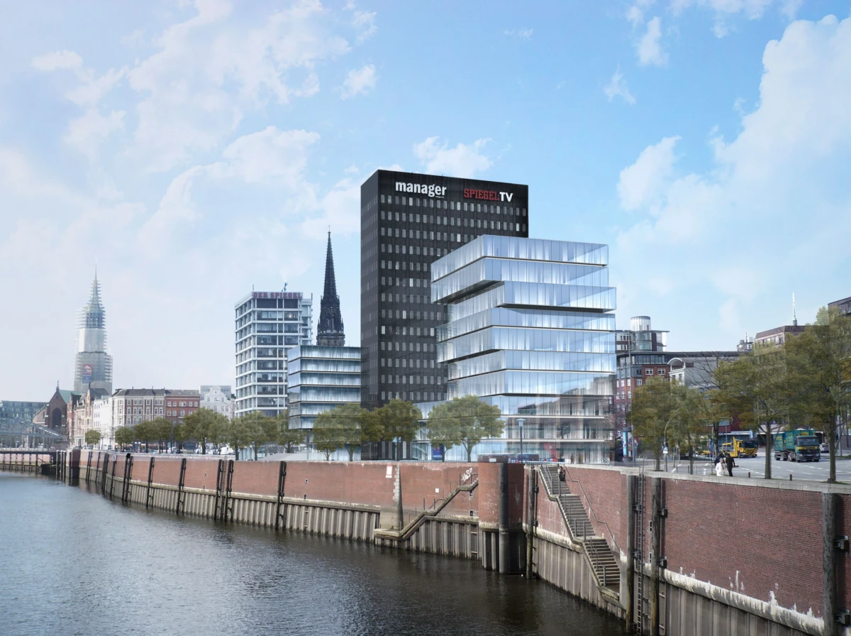 Riverside cityscape of glass office towers beside a brick quay, with trees and calm water.