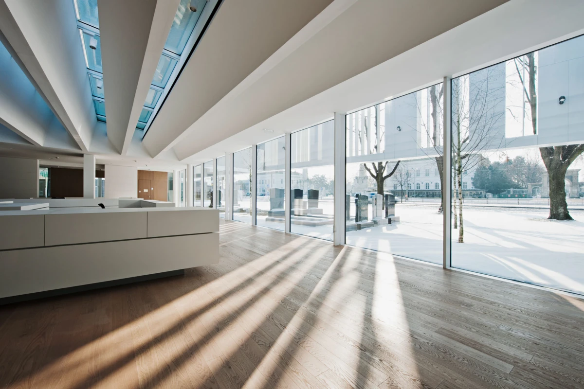 Modern empty office lobby with white reception desk, wooden floor, and floor-to-ceiling glass walls; snowy exterior visible.