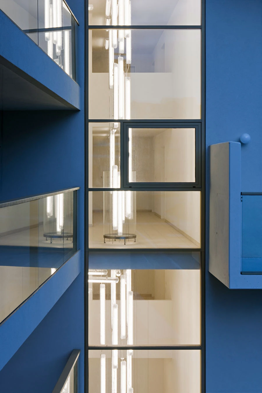 Blue glass-fronted building with a lit glass atrium and tall vertical fluorescent tubes.