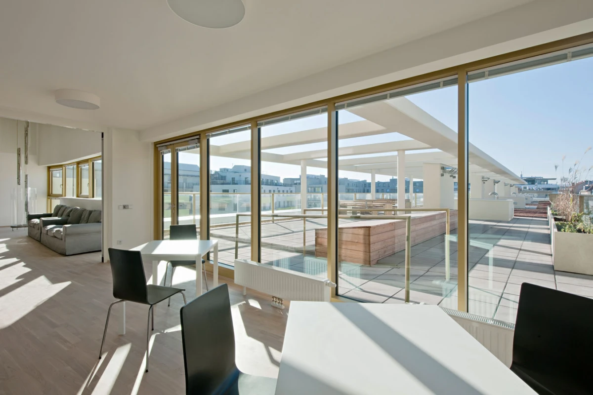 Open-plan living and dining room with floor-to-ceiling glass walls and a sunlit rooftop terrace outside.