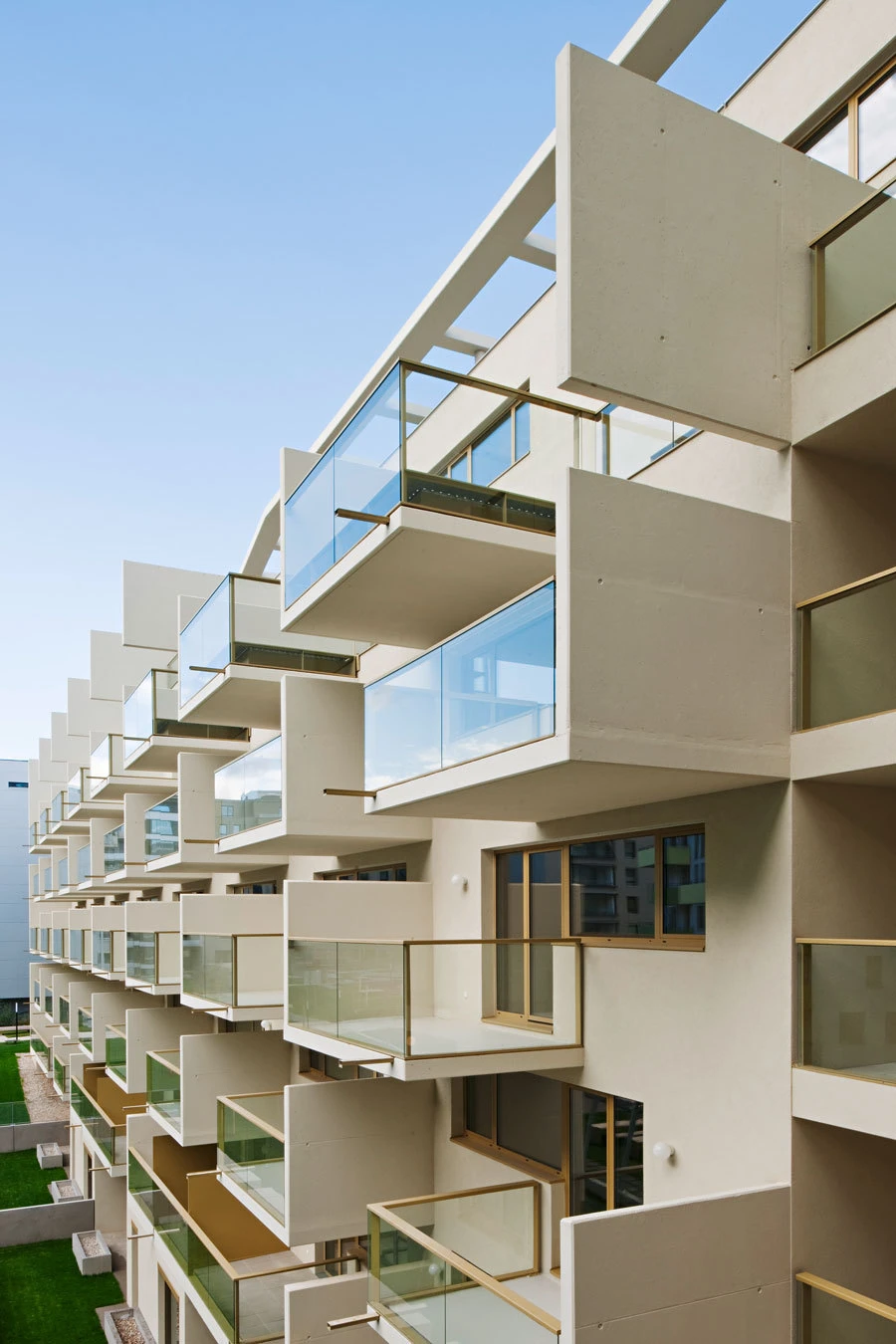 Exterior view of a modern beige apartment building with stacked glass balconies and a clear blue sky.