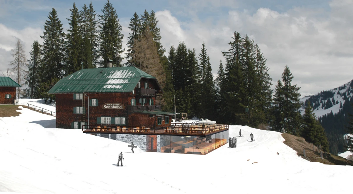 Alpine lodge with green roof on a snowy slope, wooden terrace; skiers in the foreground with conifer forest and distant mountains.