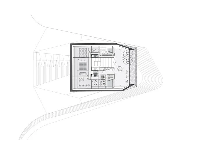 Top-down architectural floor plan of a small building, showing interior rooms and furniture within a dark border and surrounding site lines.